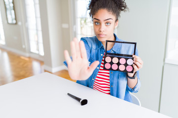 Young african american woman holding cosmetics blush palette with open hand doing stop sign with...