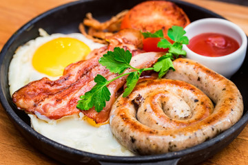 Nutritious meal with fried egg, sausage, bacon, tomato and sauce in frying pan