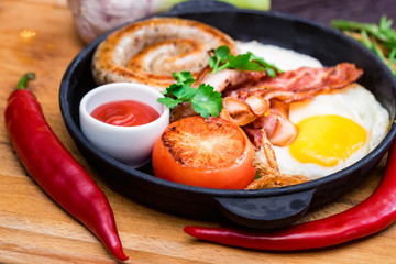 Nutritious meal with fried egg, sausage, bacon, tomato and sauce in frying pan