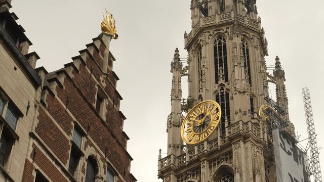 Cathedral with golden clockwork and historic building with golden ship detail, Antwerp, Belgium.
