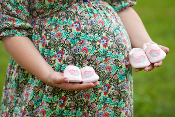Closeup of pregnant woman holding baby shoes on her belly. Twins