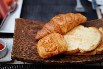 Toast and croissant on wooden plate