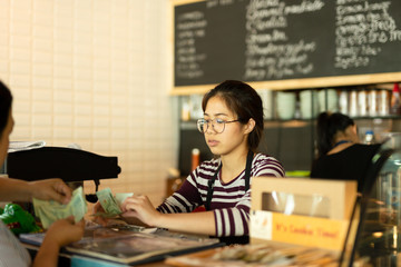 Young barista taking money from customer pay for beverage at coffee shop.