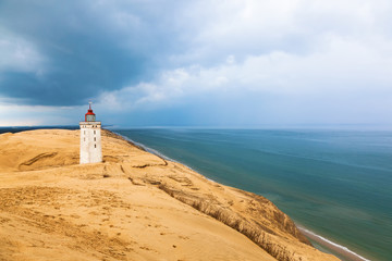 Lighthouse on Rabjerg mile on the Danish coast with storm clouds in the sky