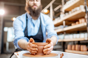 Handsome man as a potter worker in apron making clay jugs on the pottery wheel at the small manufacturing