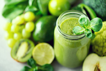 Glass jar mugs with green health smoothie, kale leaves, lime, apple, kiwi, grapes, banana, avocado, lettuce. Copy space. Raw, vegan, vegetarian, alkaline food concept. Banner