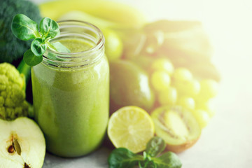 Glass jar mugs with green health smoothie, kale leaves, lime, apple, kiwi, grapes, banana, avocado, lettuce. Copy space. Raw, vegan, vegetarian, alkaline food concept. Banner