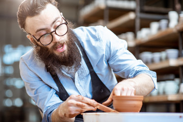 Handsome man as a potter worker in apron making clay jugs on the pottery wheel at the small...