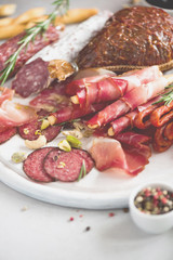 Cold smoked meat plate. Traditional italian antipasto, cutting board with salami, prosciutto, ham, pork chops, olives on grey background. Top view, copy space, flat lay