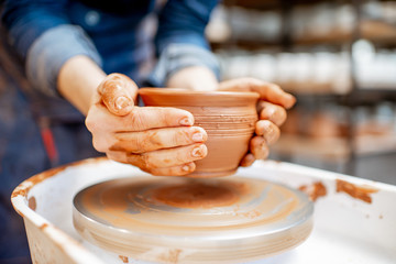 Woman taking clay jug from the pottery wheel, close-up view