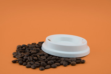 Obraz na płótnie Canvas Lid of paper coffee cup on coffee beans, orange background.
