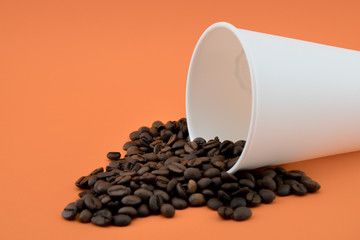 Paper coffee cup with spilled coffee beans, orange background. Coffee beans.