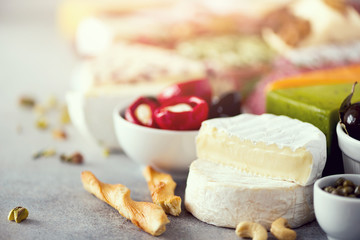 Assortment of hard, semi-soft and soft cheeses with olives, grissini bread sticks, capers, grape, on grey concrete backgound. Top view, copy space, flat lay. Cheese selection appetizer plate.