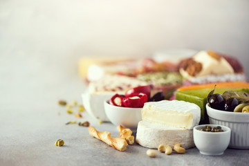 Assortment of hard, semi-soft and soft cheeses with olives, grissini bread sticks, capers, grape, on grey concrete backgound. Top view, copy space, flat lay. Cheese selection appetizer plate.