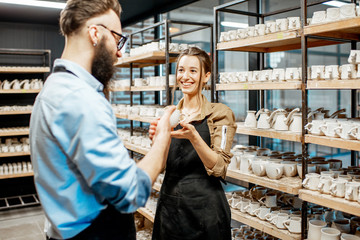 Man and woman workers checking quality of the clay products during the drying process at the pottery