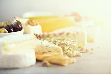 Assortment of hard, semi-soft and soft cheeses with olives, grissini bread sticks, capers, grape, on grey concrete backgound. Top view, copy space, flat lay. Cheese selection appetizer plate.