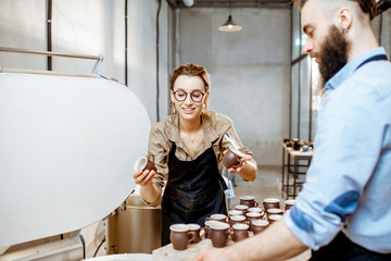 Man and woman taking baked ceramics from eleectric oven, working at the pottery manufacturing