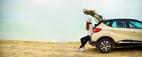 Foto op Canvas View of young woman traveler looking at sea sunset, sitting on hatchback car with the copy space. Banner © jchizhe