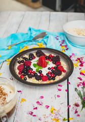 granola, fresh, nutritious breakfast with the addition of natural yoghurt, fresh and frozen fruit, and mint leaves,  on a white table decorated with spring flowers