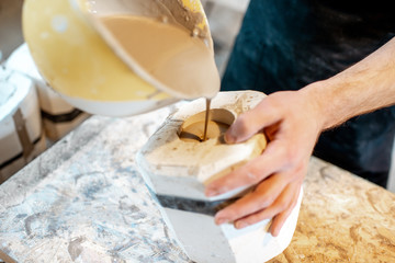 Worker pouring special liquid into the gypsum form making ceramic products at the pottery...