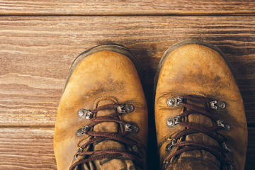 Old brown worn boots close-up on wooden background. Selective focus. Concept of travel and adventure. View from above.
