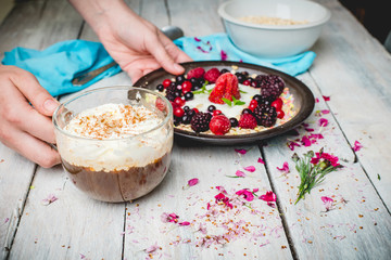 granola, fresh, nutritious breakfast with the addition of natural yoghurt, fresh and frozen fruit, and mint leaves, served on a plate held by female hands, on a white table decorated with spring flowe