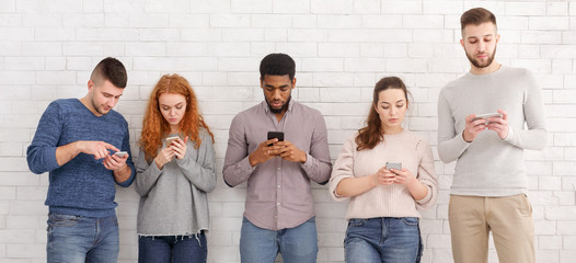 Students texting on their smartphones, leaning on wall
