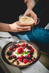 a young woman sits comfortably in an armchair in the morning sun, eats granola and drinks a coffee with whipped cream and cinnamon
