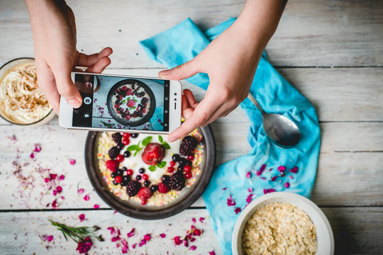 hands hold the phone, photographing colorful, healthy food on a light wooden table