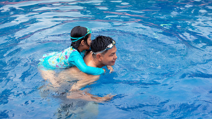 Asian father playing with his daughter in swimming pool