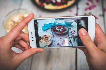 hands hold the phone, photographing colorful, healthy food on a light wooden table