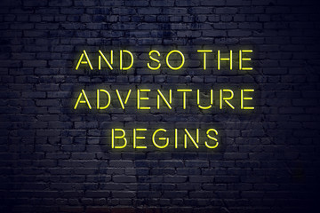 Positive inspiring quote on neon sign against brick wall and so the adventure begins