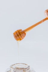 Honey dripping from wooden honey dipper on white background