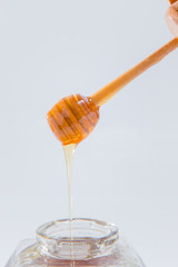 Honey dripping from wooden honey dipper on white background