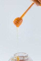 Honey dripping from wooden honey dipper on white background