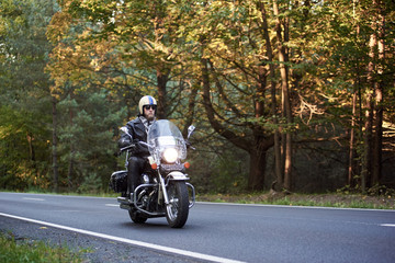 Handsome bearded biker in sunglasses, helmet and black leather clothing riding cruiser motorcycle...