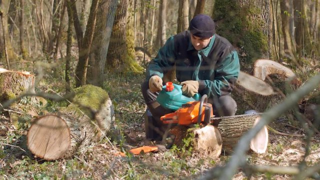 Un bucheron verse du carburant dans le r&eacute;servoir de sa tron&ccedil;onneuse