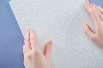 cropped view of girl reading braille text with hand isolated on violet