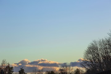 Gorgeous view of sunset on a spring day. Forest, blue sky and clouds converging on the horizon. Beautiful colorful nature background.