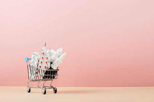 Shopping cart loaded with pills on a pink yellow background. The concept of medicine and the sale of drugs. Copy space.