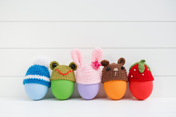 Easter Egg. A row of Easter eggs with cute crochet sweater hat isolated on the white wooden background. Creative ideas for Easter eggs decoration.