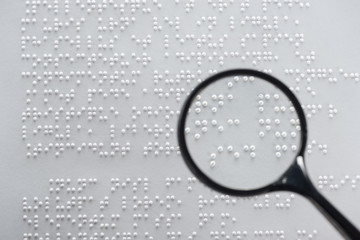top view of braille text on white paper with magnifying glass