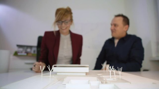 Two architects giving high five behind a model house in office