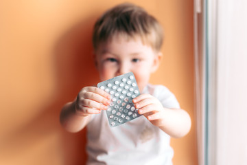 A small child toddler baby boy holds a plate with pills in his hands selected focus on pills kid...