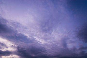 Obraz premium Dramatic evening sky with purple and blue dark clouds like Cirrocumulus, Altocumulus and Cumulus. Small crescent moon behind cloudscape. Wind and motion. 