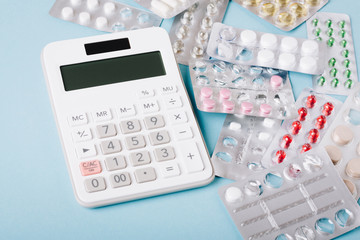 White calculator and pills on a blue background as a symbol of paid (expensive) medicine