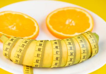 Sliced orange , banana and centimeter on a white plate . Diet concept.