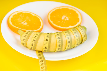 Sliced orange , banana and centimeter on a white plate . Diet concept.