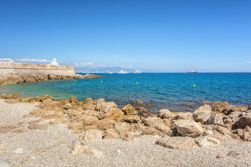 The old city wall along the coast of the French town of Antibes with above it the head of the famous artworks The Nomad