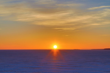 The sunset or sunrise. The cloudy sky cloured in red, orange, crimson, purple, violet and blue bright and vivid coloures with setting or rising sun over the sea, lake or bay covered with ice and snow